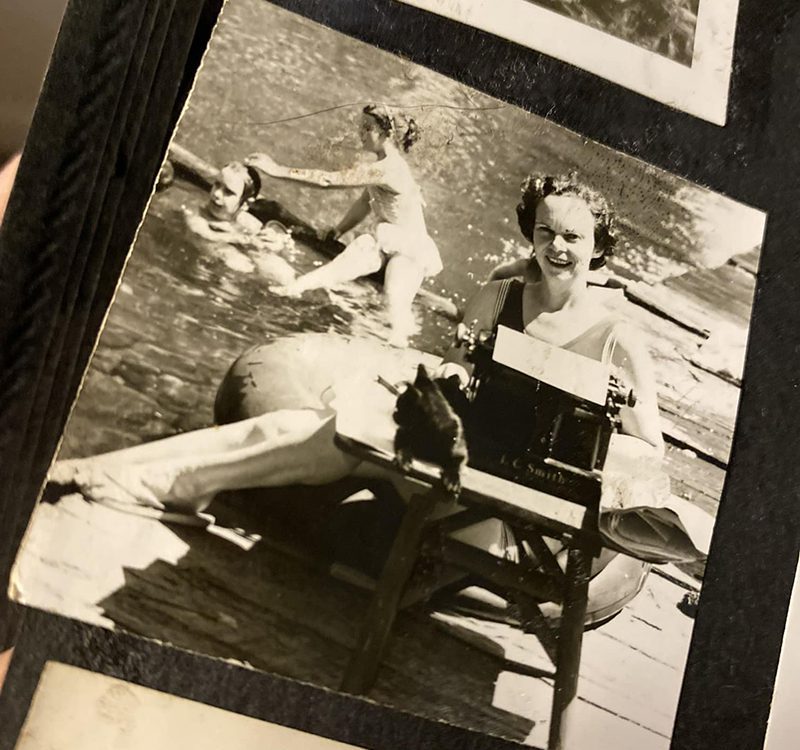 Authors mom with typewriter on lake dock with kids swimming behind her